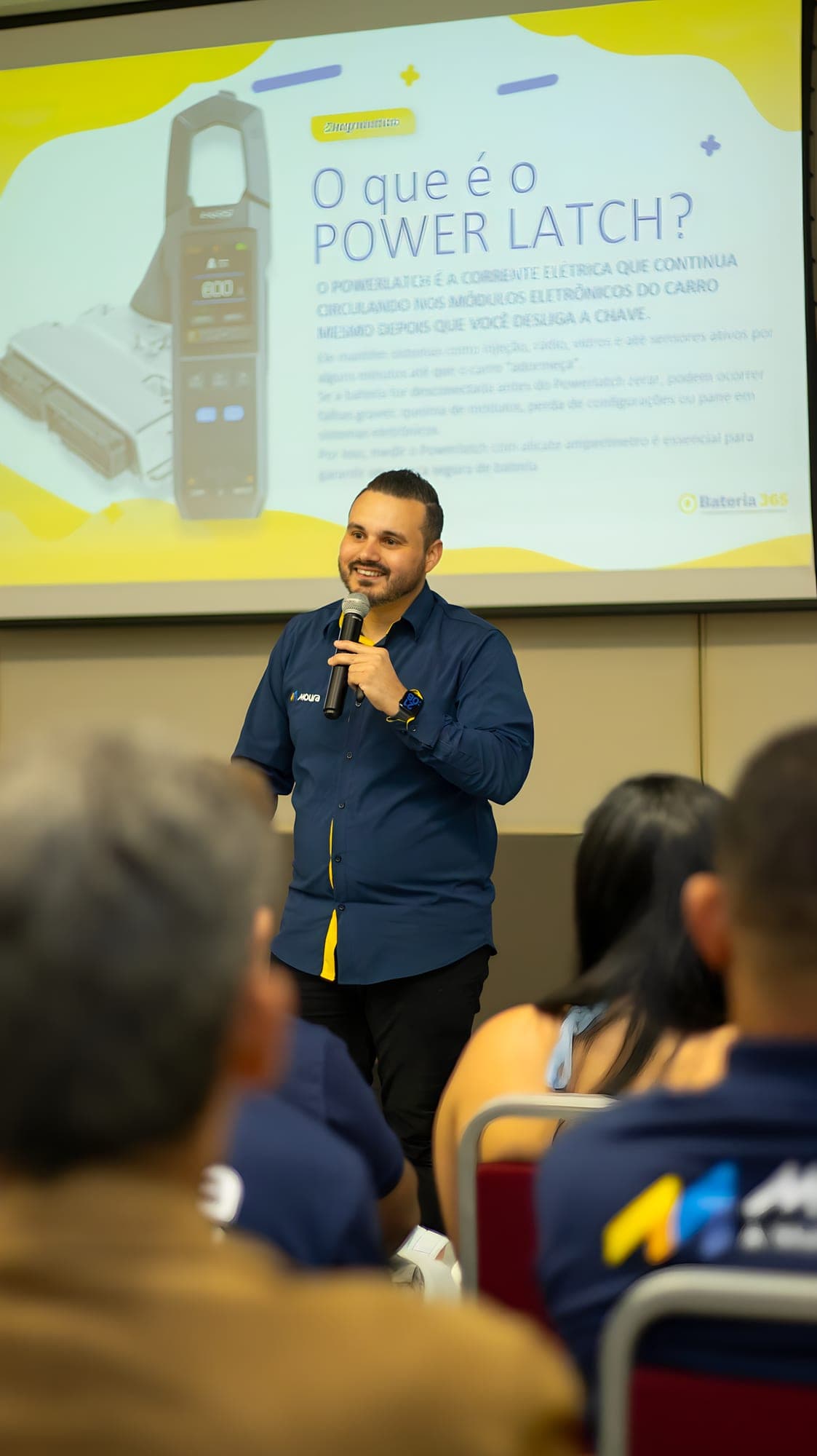 Rafael explicando o que é o Power Latch para a plateia, com o slide no telão.