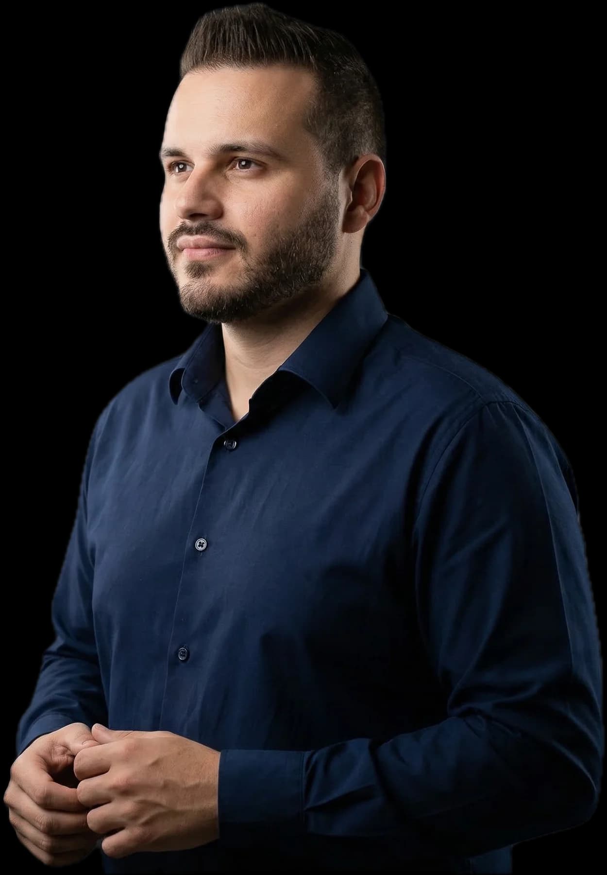 Rafael André em retrato de estúdio, de camisa azul-marinho, olhando para o lado com as mãos juntas.